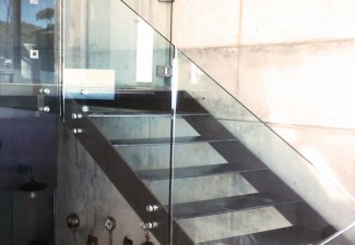 Barandilla de vidrio templado a, montado sobre escalera de hierro oxidado, con soportes de acero inoxidable soldados.